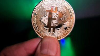 a hand holding a bit coin in front of a green light