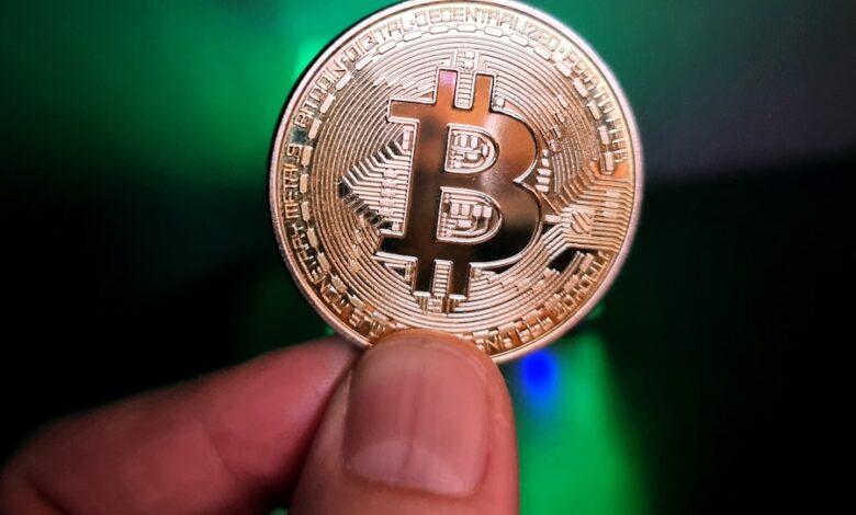 a hand holding a bit coin in front of a green light