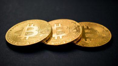 three gold-colored bitcoins on black surface