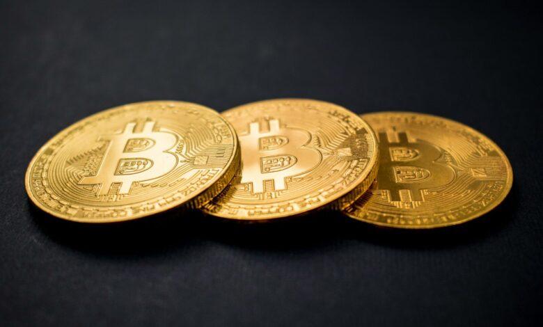 three gold-colored bitcoins on black surface